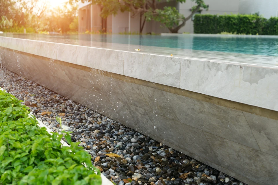 Scène extérieure de piscine moderne avec cascade d'eau s'écoulant le long d'un mur de pierre naturelle