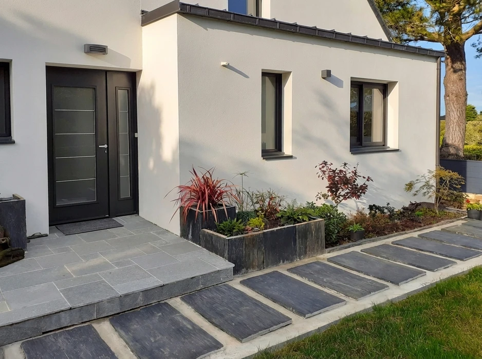 Équipe de professionnels en tenue de travail et équipement de sécurité (gilets, casques) réalisant les travaux d'aménagement extérieur d'une terrasse ou d'un jardin. Scène montrant un ou plusieurs collaborateurs engagés dans la construction, maçonnerie ou préparation du sol. L'image doit clairement montrer du travail en cours, des outils, et démontrer l'intervention de salariés de l'entreprise sur un chantier d'aménagement extérieur.